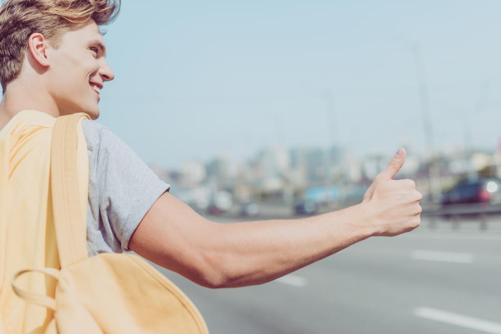 uśmiechnięty mężczyzna młody autostopem na drodze - Zdjęcie, obraz