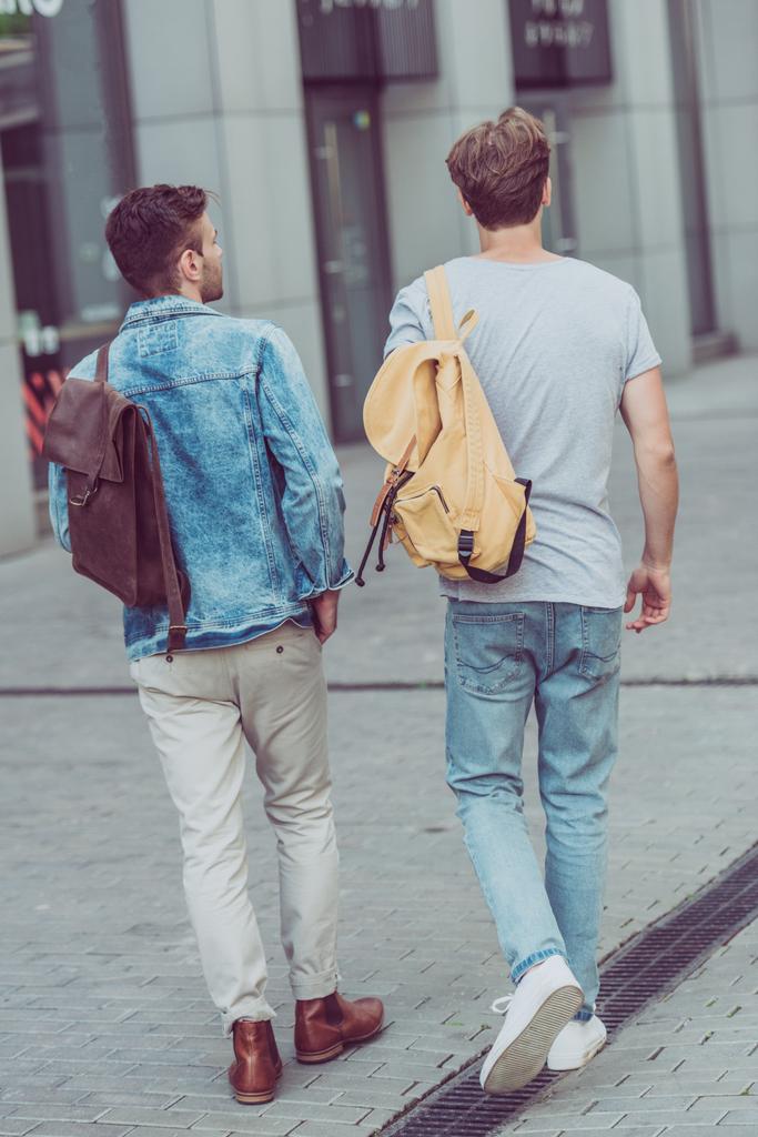 back view of travelers with backpacks walking on city street - Photo, Image