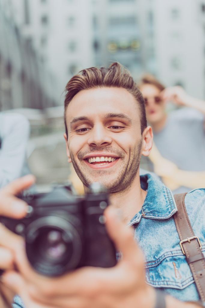 вибірковий фокус усміхненого чоловіка з фотоапаратом, що подорожує у новому місті
 - Фото, зображення