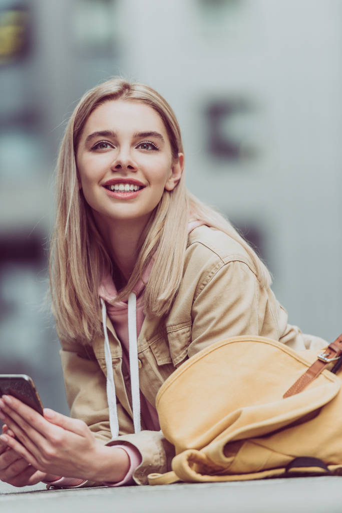 sorrindo menina loira com mochila usando smartphone
 - Foto, Imagem