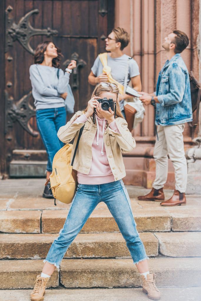 beautiful girl taking photo of city on camera with friends behind - Photo, Image