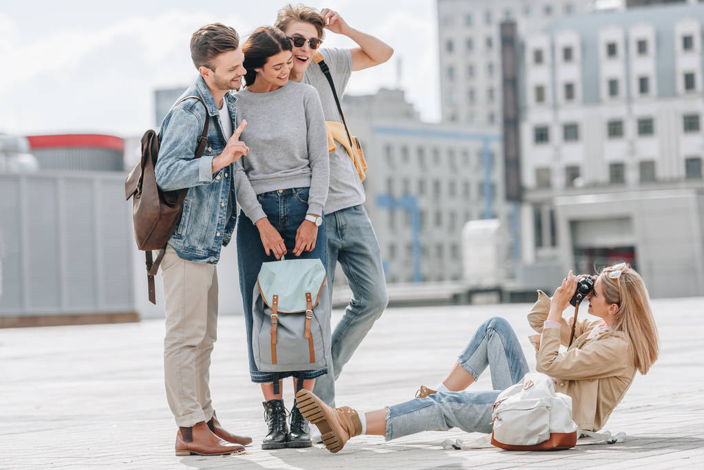 Mädchen sitzt auf der Straße und fotografiert glückliche Freunde - Foto, Bild
