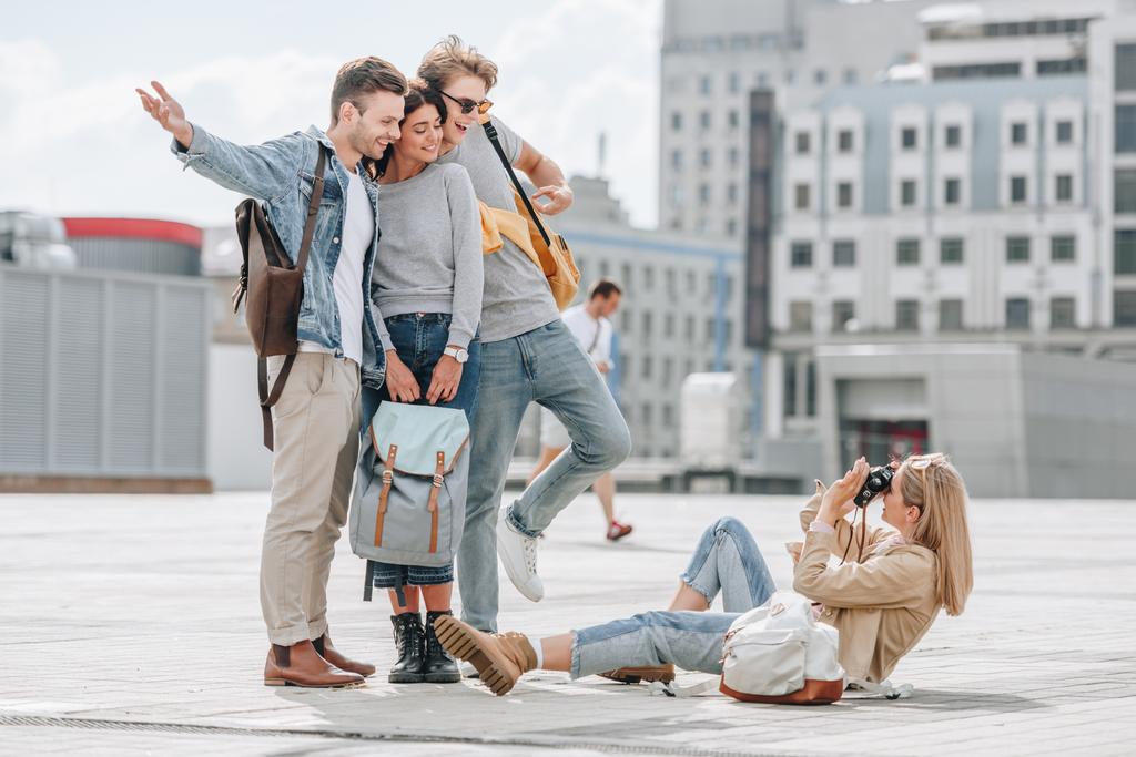 meisje zittend op straat en nemen foto van vrolijke reizigers in stad - Foto, afbeelding