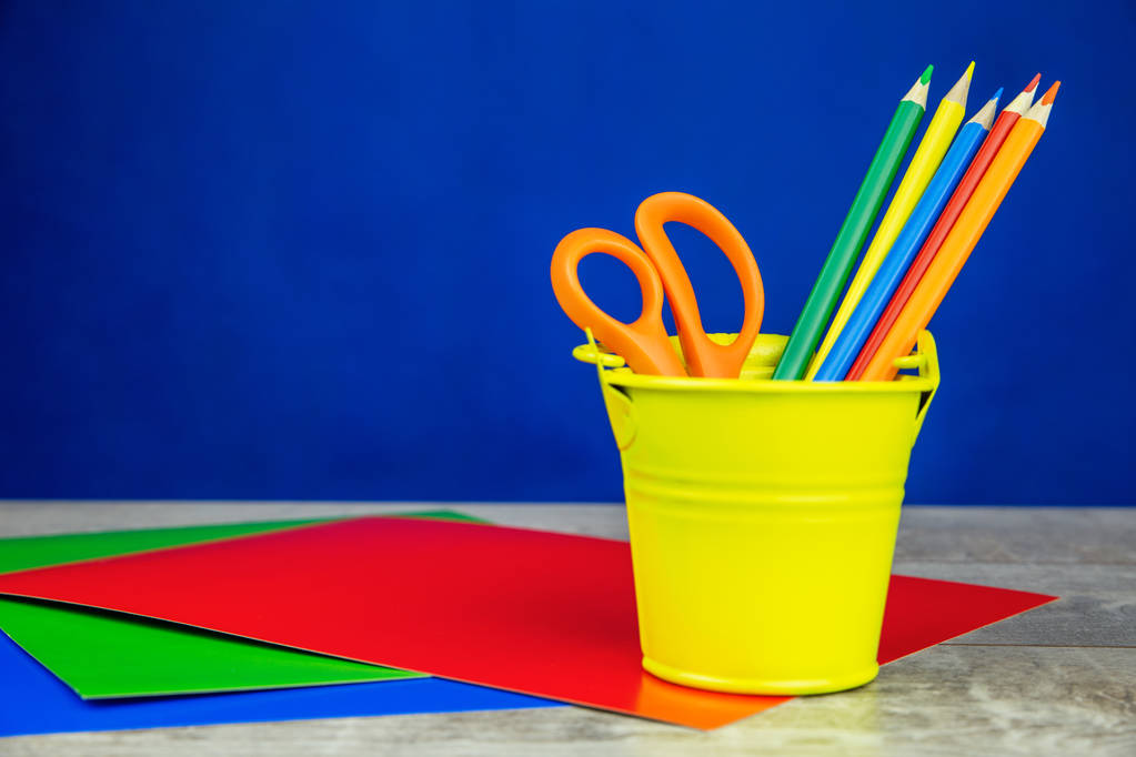 Kleurrijke potloden en vellen papier op witte houten bureau en donker blauwe achtergrond - Foto, afbeelding
