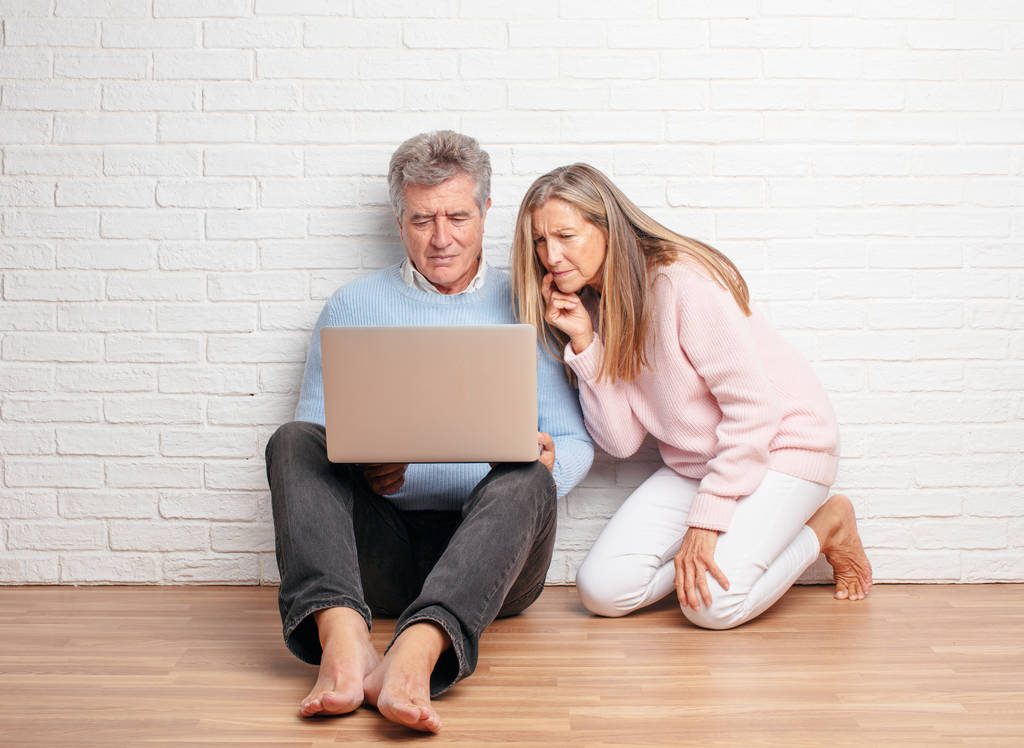 casal muito sênior sentado em seu chão casa com um laptop
 - Foto, Imagem