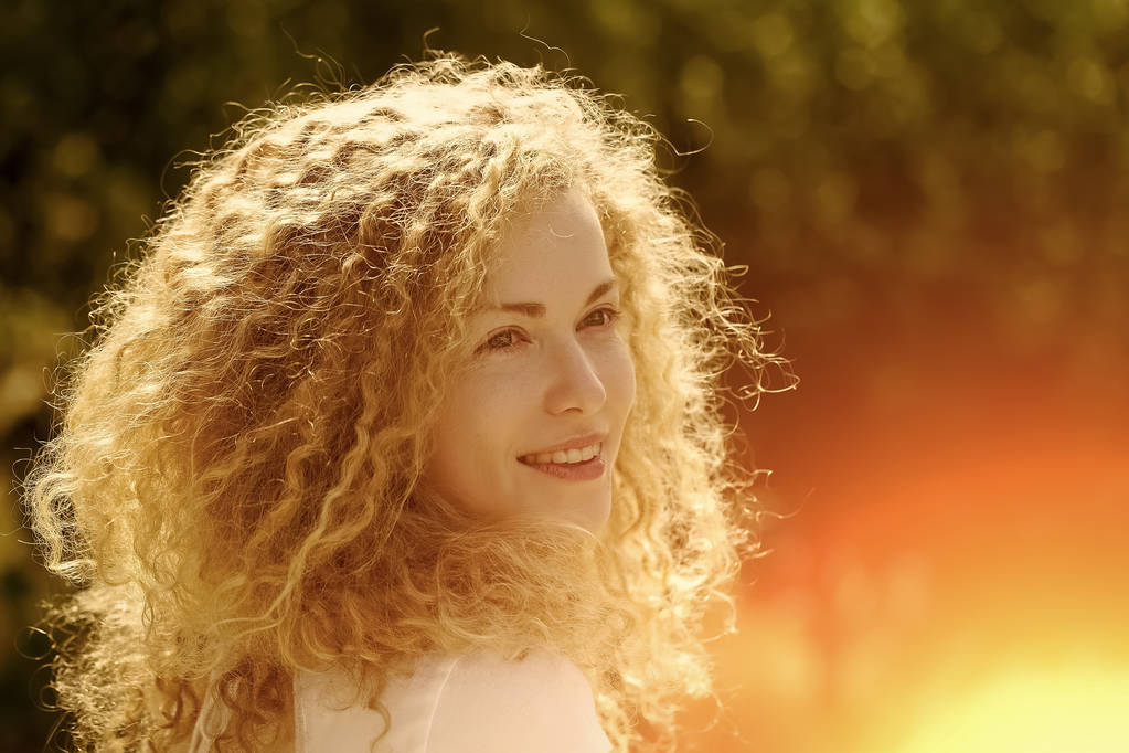 Portret van een vrij peinzende schattige blonde jonge lachende vrouw met lang krullend haar en zoete blije gezicht op zoek weg zonnige dag buiten op natuurlijke achtergrond, horizontale afbeelding - Foto, afbeelding