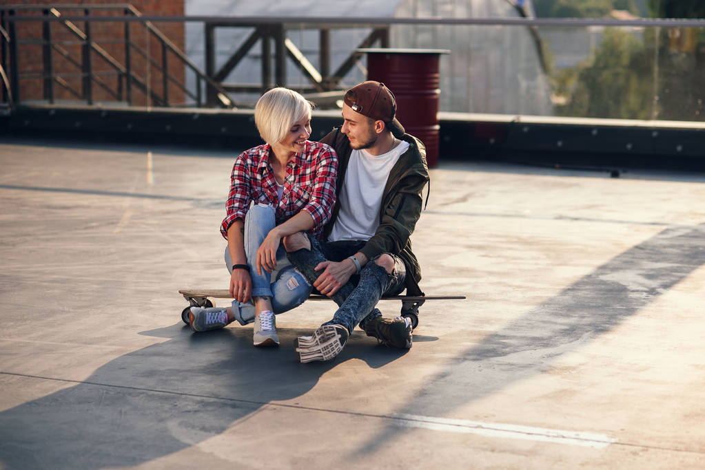 Giovane bella coppia divertirsi con lo skateboard longboard sul tetto dell'edificio industriale. Moderno concetto di stile di vita urbano attivo
. - Foto, immagini