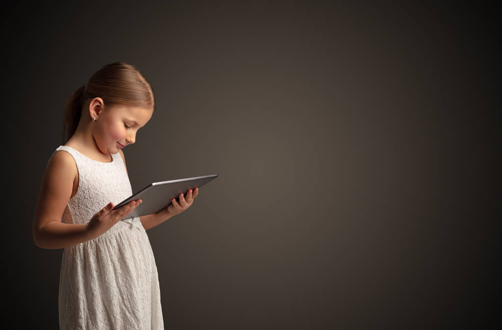 Nettes kleines Mädchen mit Tablet mit dunklem Hintergrund - Foto, Bild