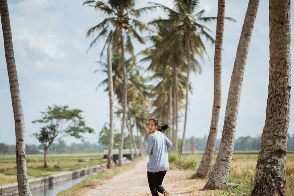 μια γυναίκα που έτρεξε σε πλευρά δέντρα καρύδας, κοιτάζοντας πίσω σε κάμερα - Φωτογραφία, εικόνα