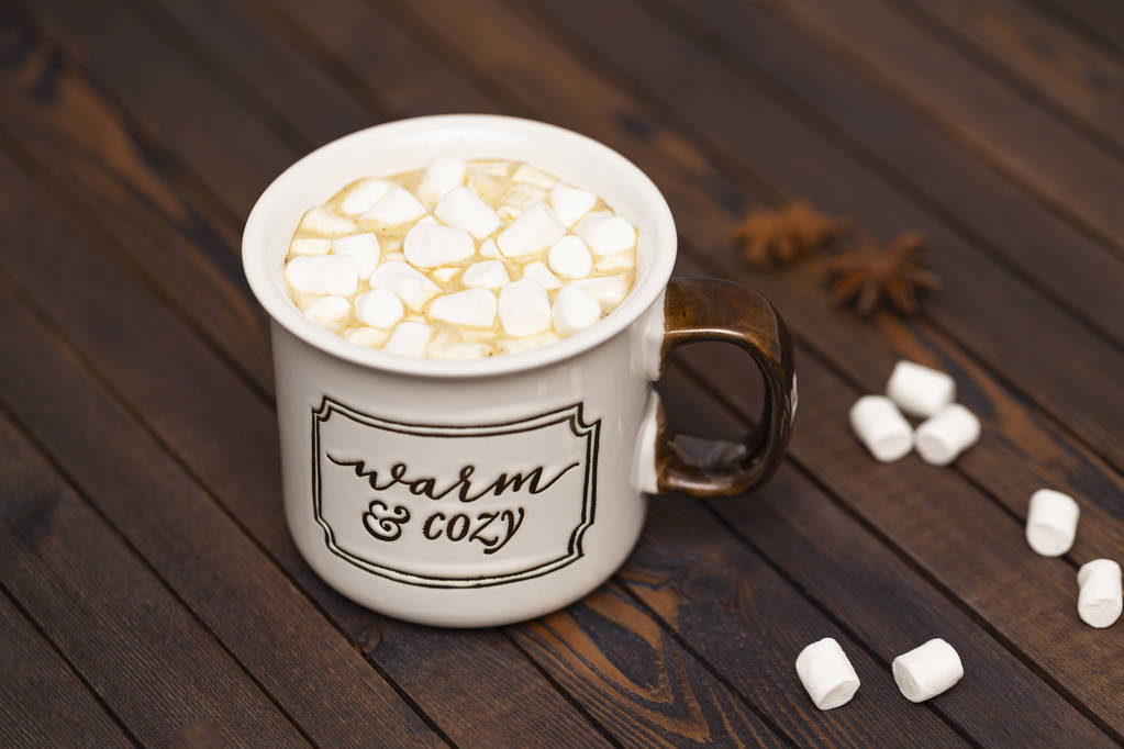 Cacau com marshmallows em um fundo de madeira em uma xícara com a inscrição "Quente e acolhedor
" - Foto, Imagem
