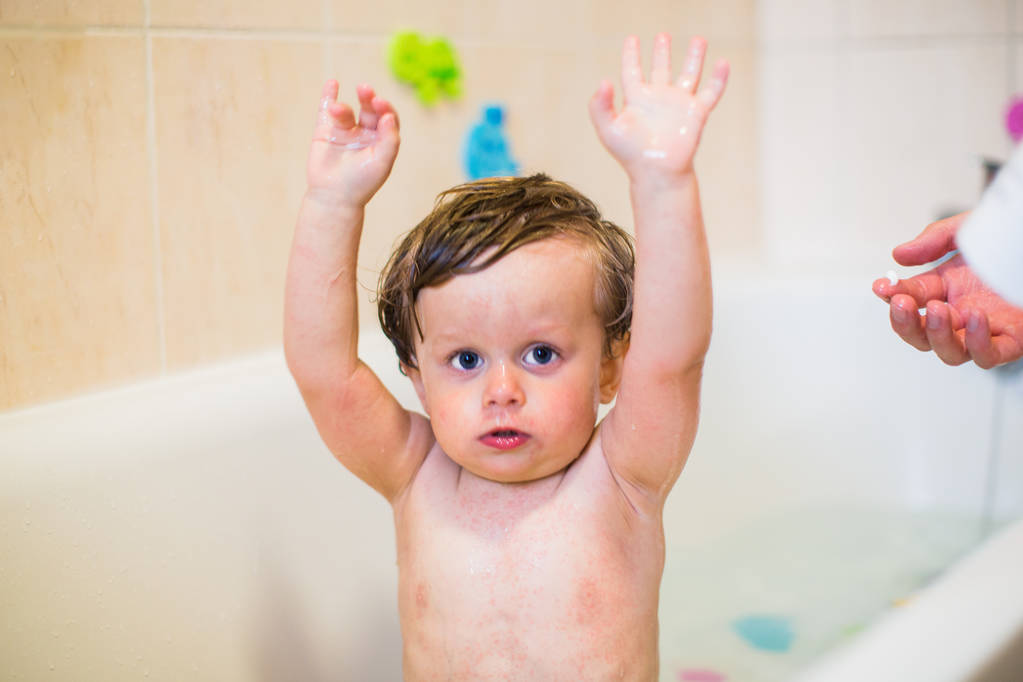 Trochę chory chłopiec siedzi w wannie i utrzymuje jego ręce do góry rodzic może umyć go ponieważ jego ciało ma wysypki, wewnątrz - Zdjęcie, obraz