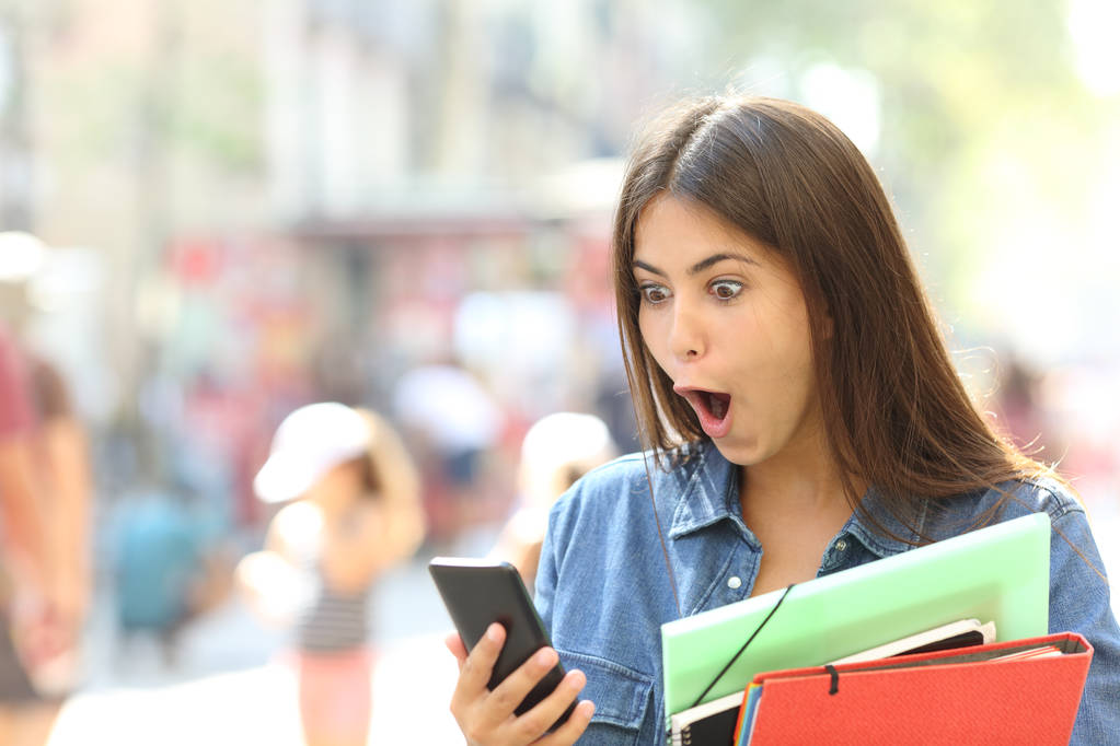 Sorpreso studente ragazza guardando contenuti smart phone in strada
 - Foto, immagini