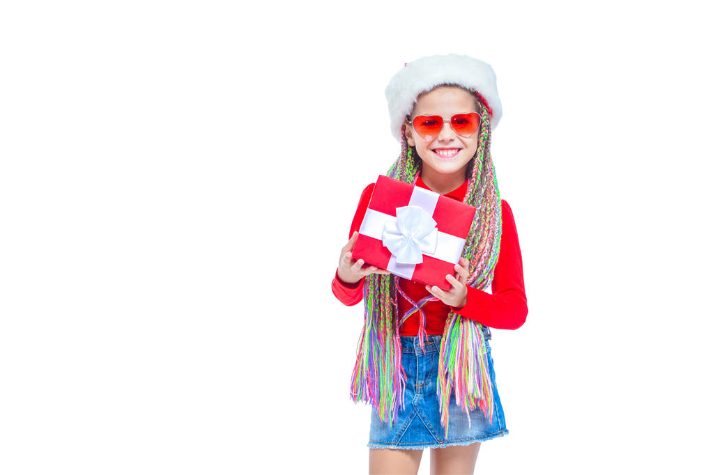 Dziewczyna w kapeluszu Santas. Portret cute dziewczynka trzymając pudełko Boże Narodzenie obecny, małe dziewczynki przytulić jej prezent z wyrażenie zadowolony i zabawa na białym tle. Prezent świąteczny - Zdjęcie, obraz
