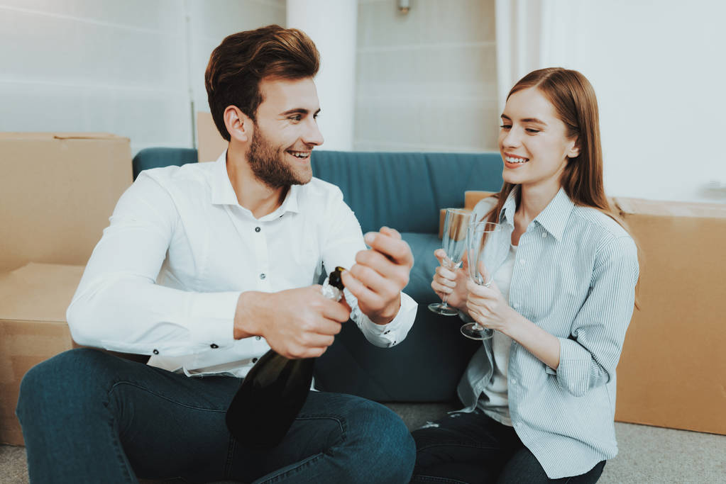 Young Couple In New Apartment. Champagne Celebrating. Love Each Other. Cheerful Sweethearts. New Life. Personal Flat. Happy Family. Domestic Life. Orange Boxes. Siting On The Floor. - Photo, Image