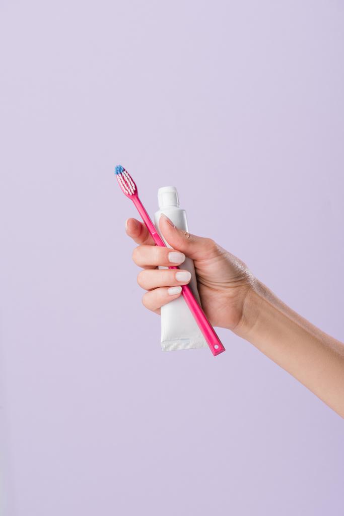 tiro recortado de mujer sosteniendo cepillo de dientes y tubo de pasta aislado en púrpura
 - Foto, imagen