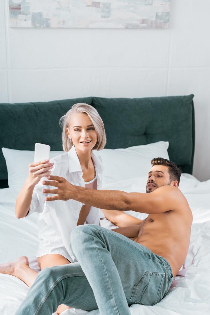 Verspieltes junges Paar beim gemeinsamen Selfie im Schlafzimmer - Foto, Bild