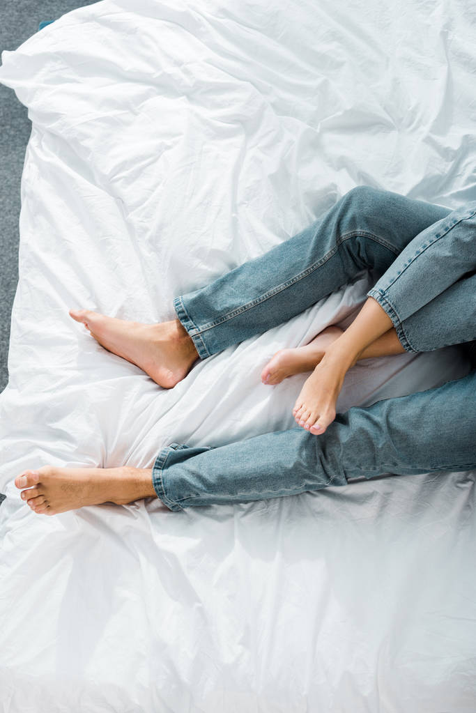 обрезанный образ молодой пары в джинсах лежащих на кровати в спальне
 - Фото, изображение