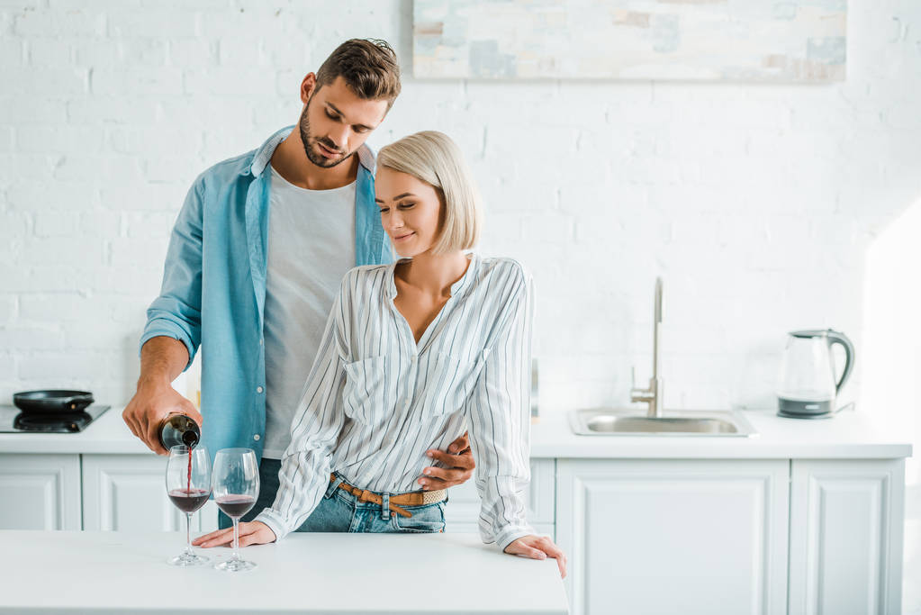 guapo novio abrazando novia de vuelta en la cocina y verter vino de botella
 - Foto, Imagen