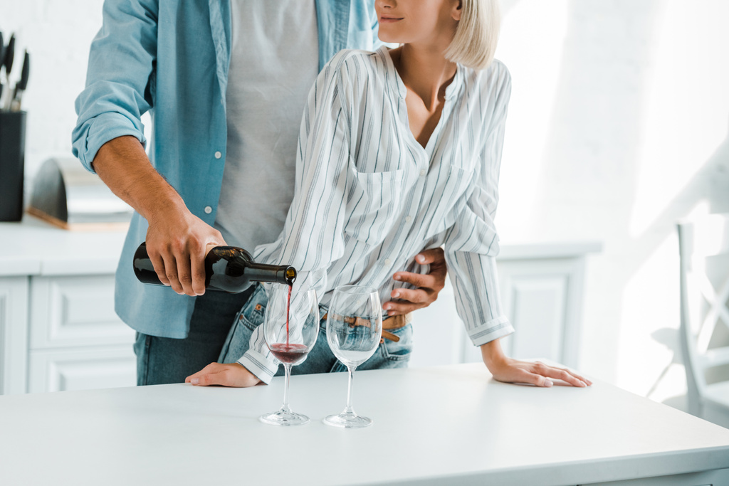 immagine ritagliata di fidanzato abbracciare la ragazza da indietro in cucina e versando vino dalla bottiglia
 - Foto, immagini