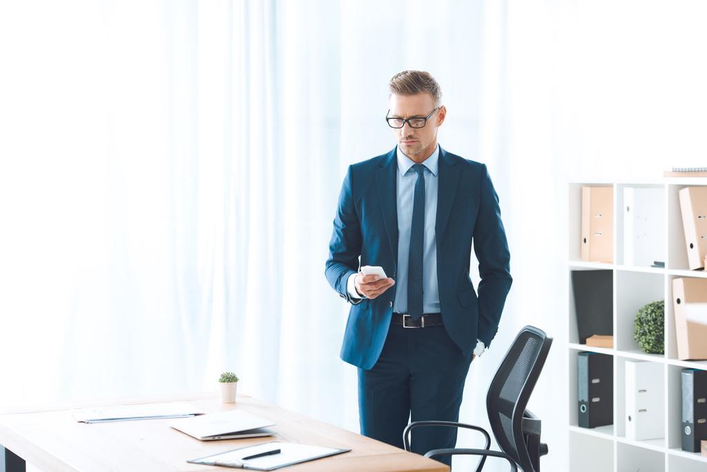 bel homme d'affaires en lunettes et vêtements formels en utilisant smartphone sur le lieu de travail
 - Photo, image
