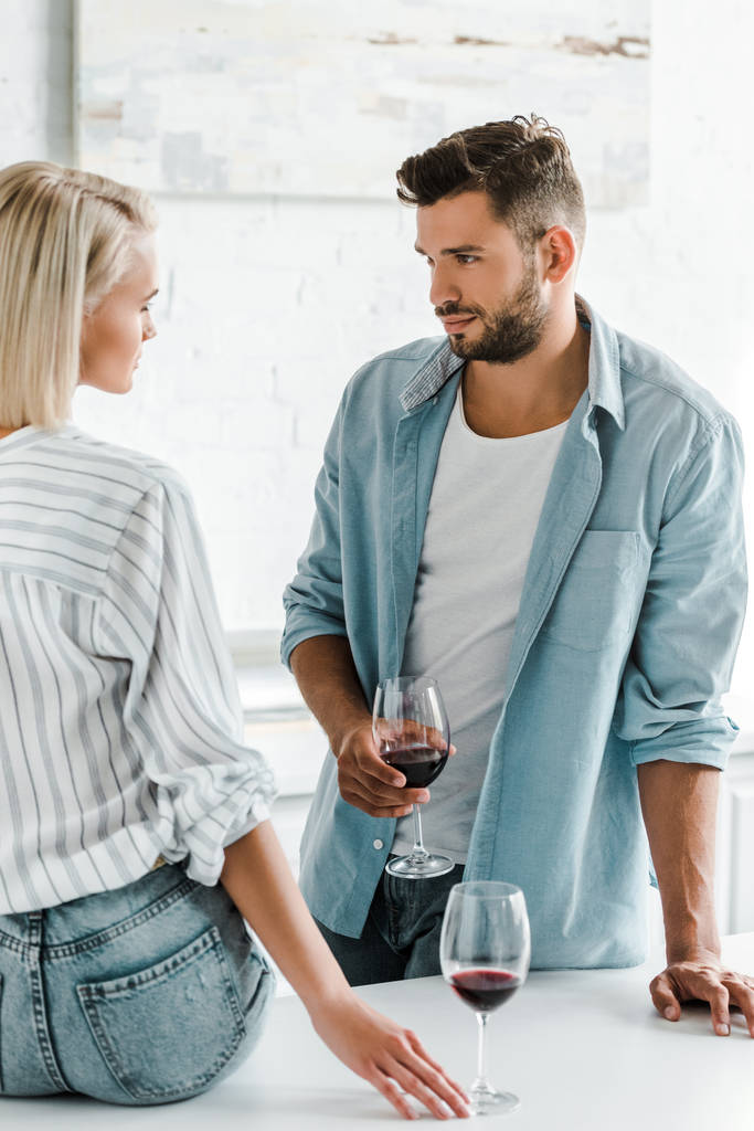 giovane coppia che si guarda, fidanzato che tiene un bicchiere di vino in cucina
 - Foto, immagini