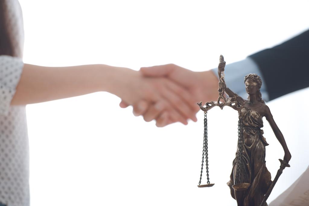 vista de cerca de la estatua de la justicia dama y abogado con el cliente en blanco estrechando las manos detrás
 - Foto, imagen