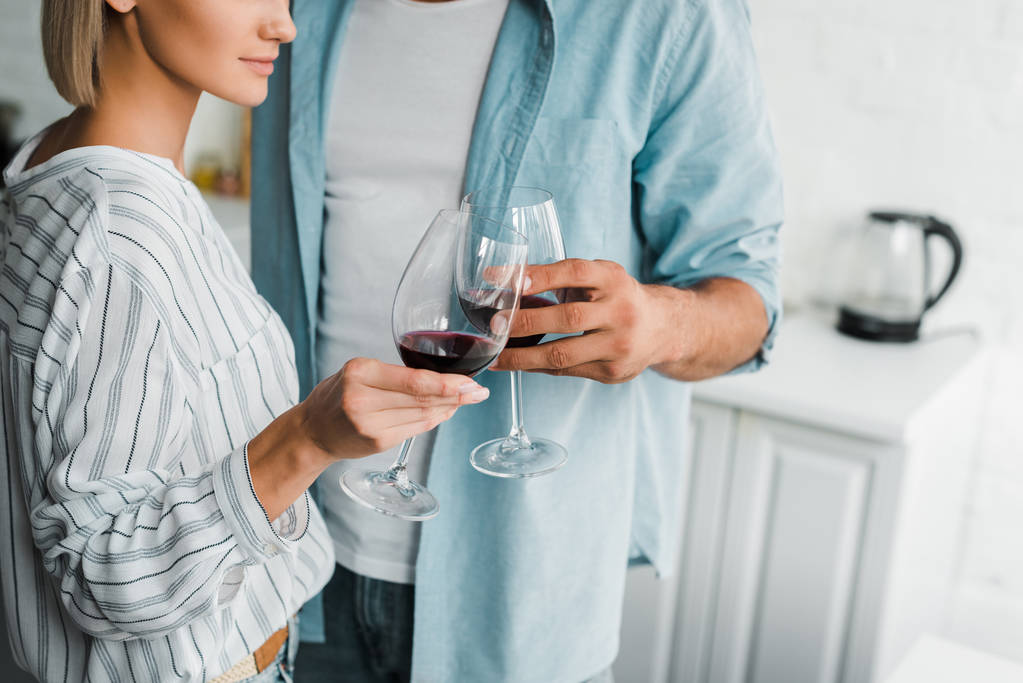 imagen recortada de pareja joven tintineo con gafas de vino en la cocina
 - Foto, imagen