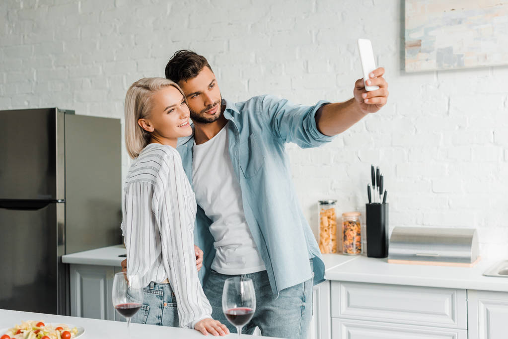 Fröhliches junges Paar macht Selfie mit Smartphone in Küche - Foto, Bild