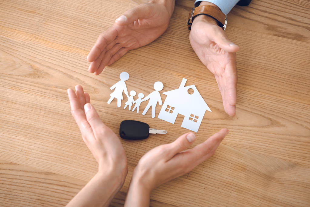 partial view of insurance agents and female hands with house, family paper models and car key on wooden tabletop - Photo, Image