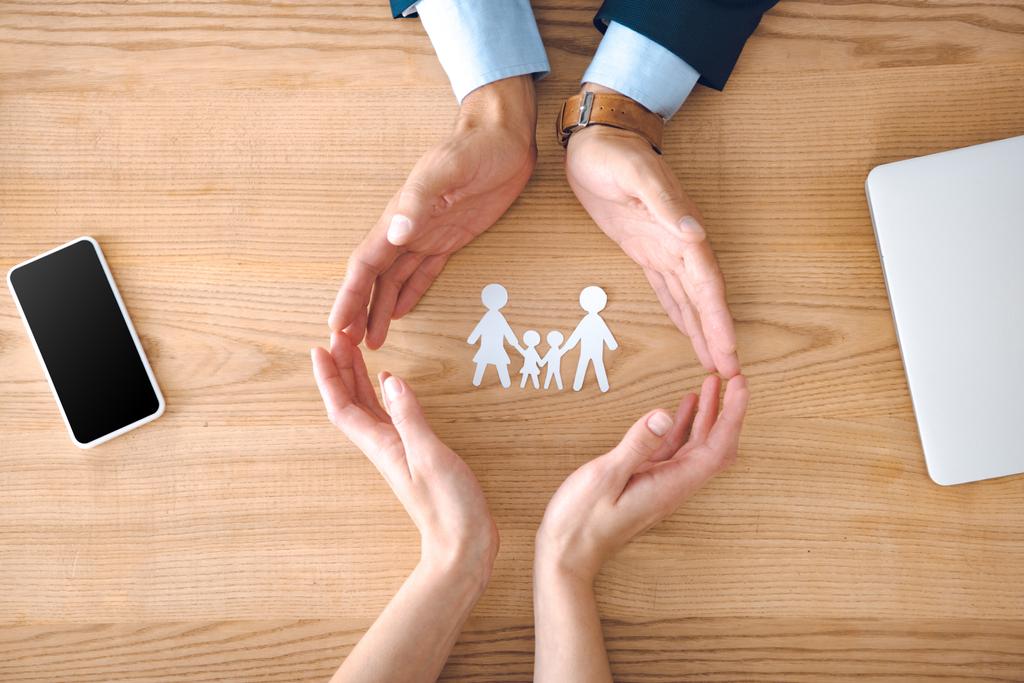 partial view of insurance agents and female hands with family paper model on wooden tabletop, family insurance concept - Photo, Image