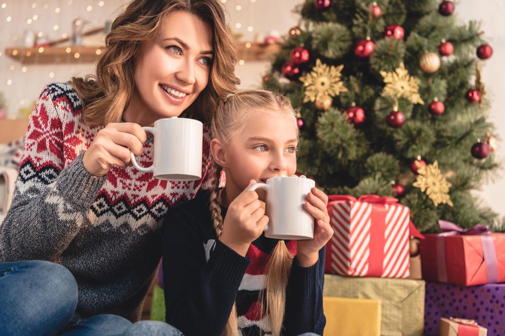 feliz madre e hija bebiendo cacao cerca del árbol de Navidad en casa
 - Foto, Imagen