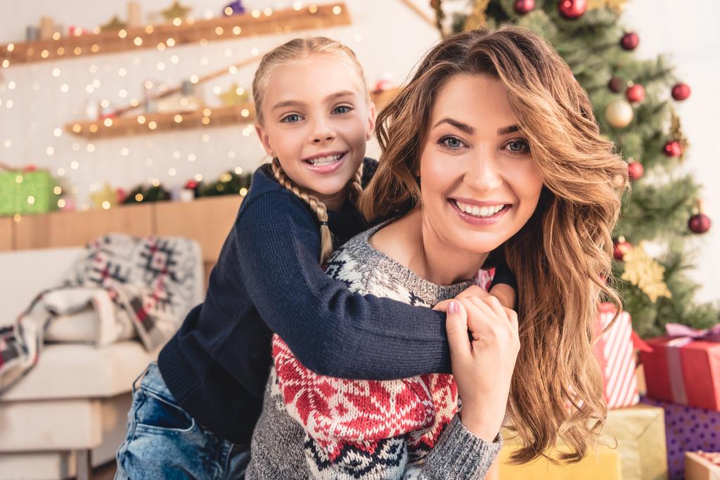 onnellinen äiti antaa reppuselässä tytär kotona ja he katsovat kamera, joulu käsite
 - Valokuva, kuva