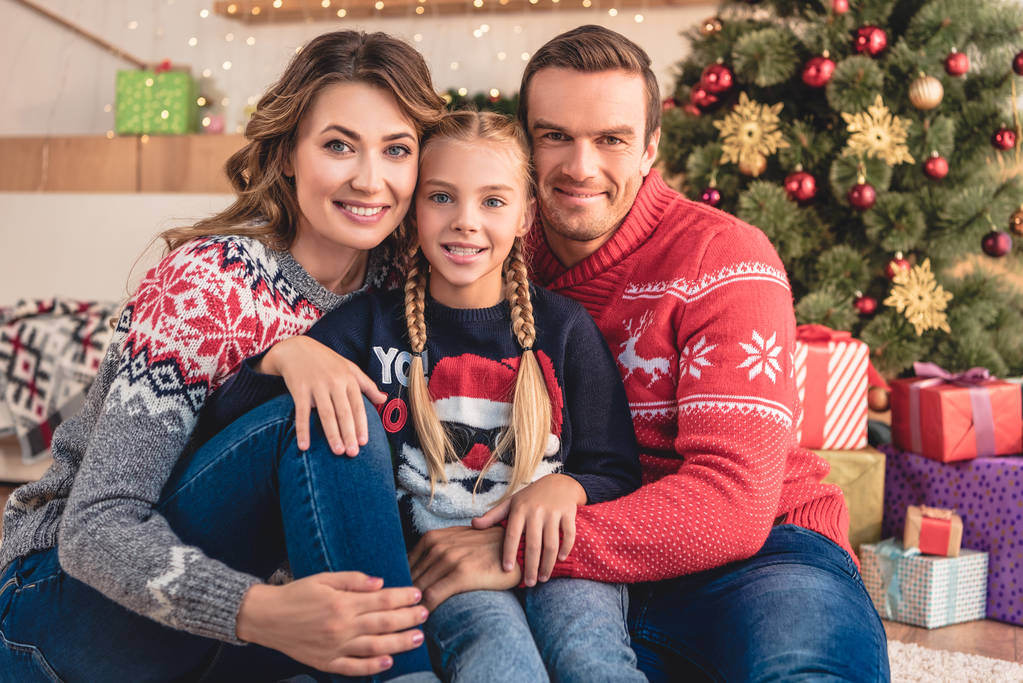 pais sorridentes e filha abraçando e sentado perto da árvore de natal e presentes em casa
 - Foto, Imagem