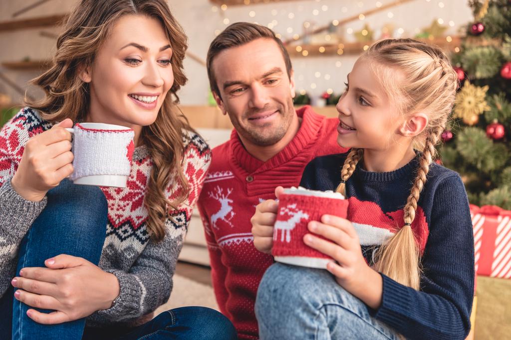 vidám szülők és lánya karácsonyi ülő földre otthon cappuccino csésze - Fotó, kép