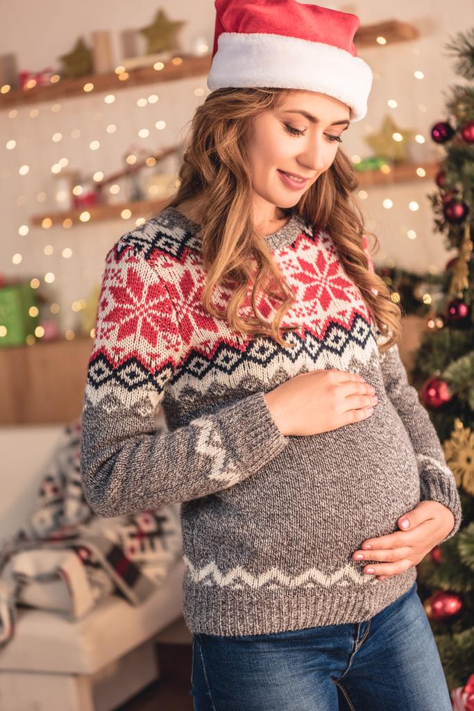 attrayant femme enceinte dans santa chapeau toucher le ventre à la maison
 - Photo, image