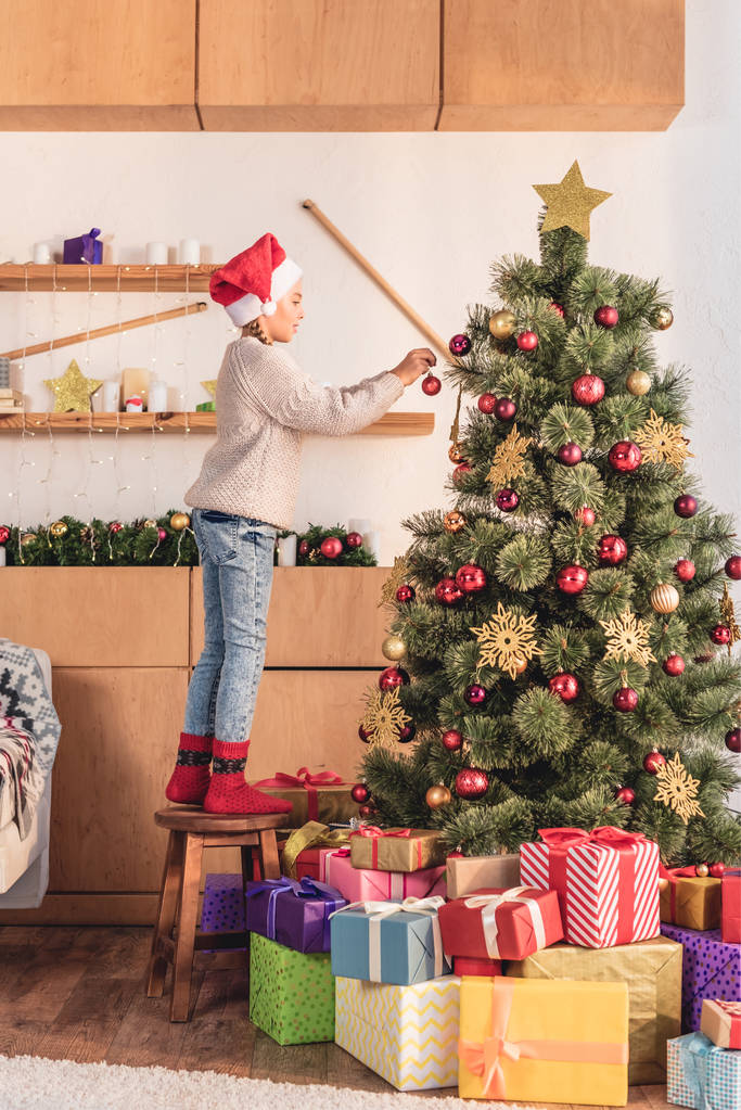 boční pohled na rozkošné nedospělý kluk v santa klobouk dekorační vánoční stromeček doma - Fotografie, Obrázek