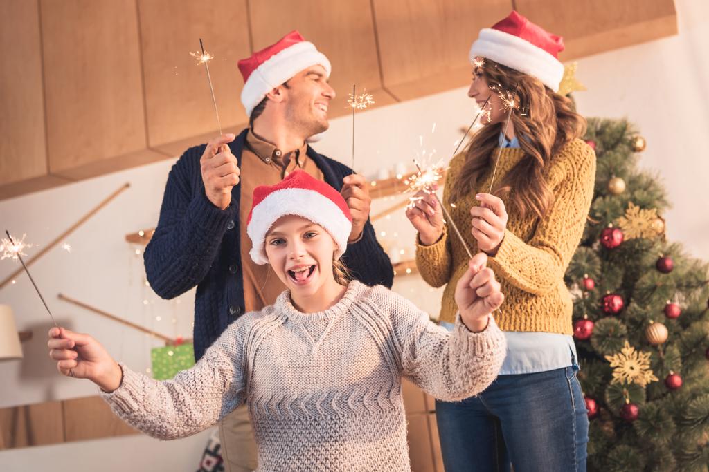 vidám család ünnepli csillagszórók otthon a karácsonyfa santa kalap - Fotó, kép