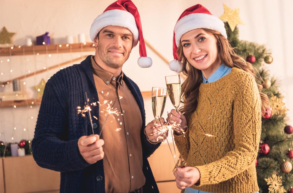 feliz pareja en sombreros de santa celebrando la Navidad con copas de champán y bengalas
 - Foto, Imagen