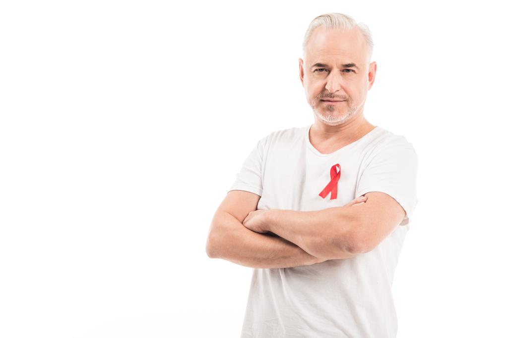 όμορφος ώριμος άνδρας σε κενό λευκό t-shirt με aids ευαισθητοποίησης κόκκινη κορδέλα βλέπουν φωτογραφική μηχανή με σταυρωμένα χέρια απομονωθεί σε λευκό - Φωτογραφία, εικόνα