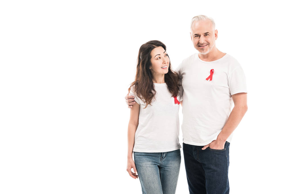 Lächelndes erwachsenes gemischtrassiges Paar in weißen T-Shirts mit Hilfsmitteln Bewusstsein rote Bänder umarmen isoliert auf weiß - Foto, Bild