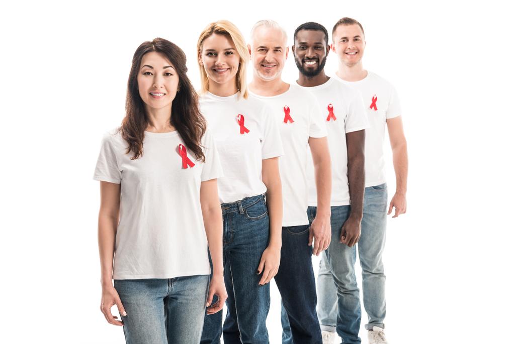 grupo sonriente de personas en camisetas blancas en blanco de pie en fila con cintas rojas de conciencia de sida aisladas en blanco
 - Foto, imagen