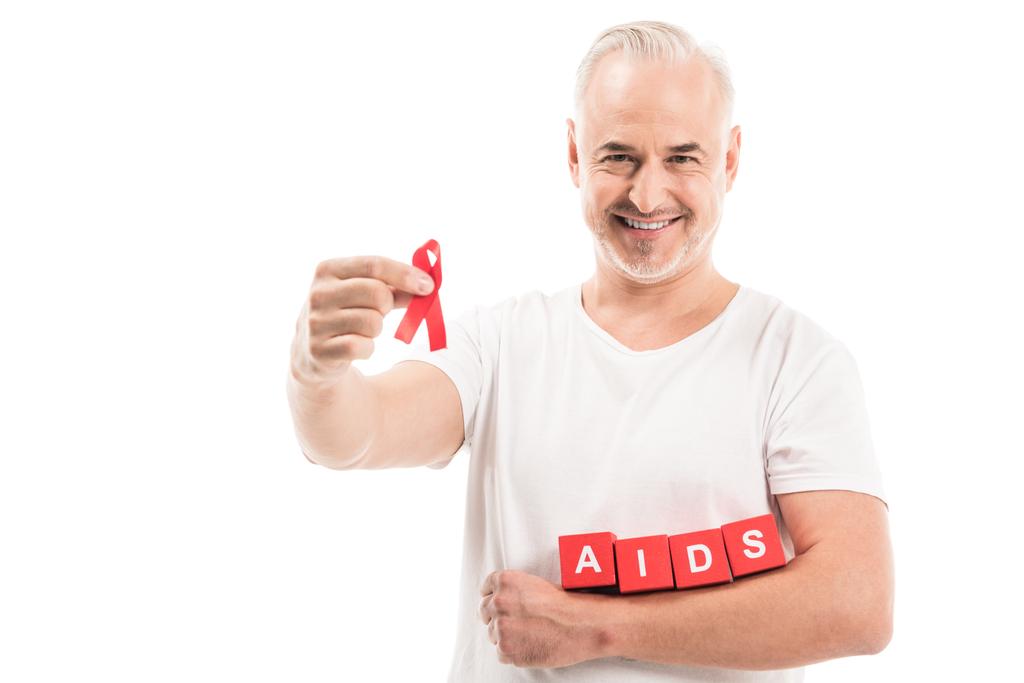 glücklicher reifer Mann in weißem T-Shirt mit Aids-Bewusstsein rotes Band und Blöcke mit Aids-Schriftzug isoliert auf weißem Grund - Foto, Bild