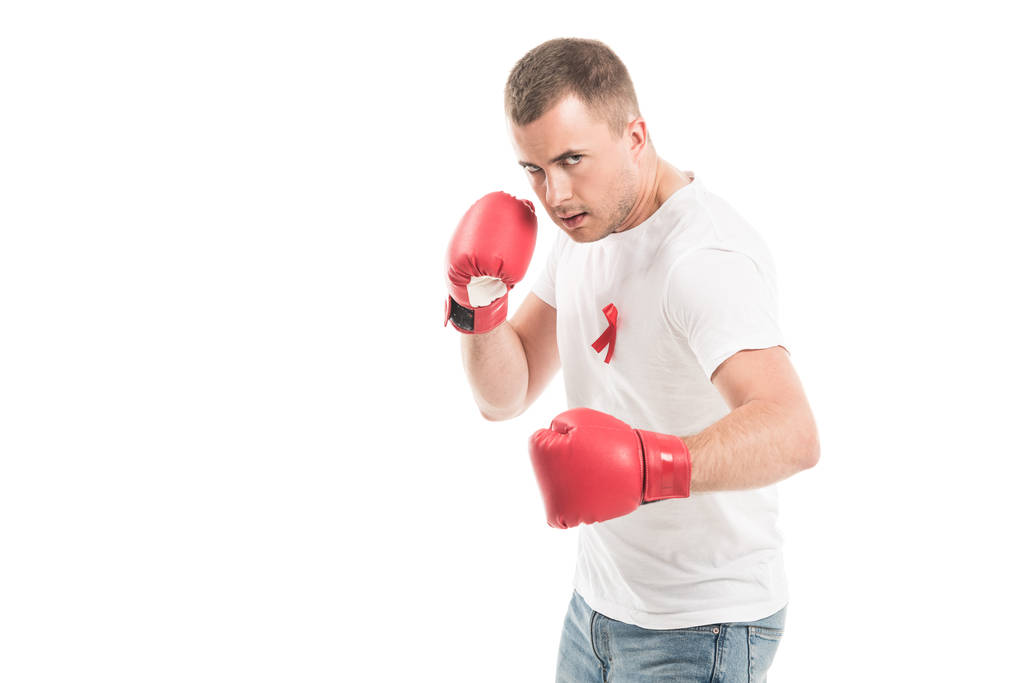 sterke knappe man in lege witte t-shirt met aids bewustzijn rood lint en bokshandschoenen geïsoleerd op wit, bestrijding van aids concept - Foto, afbeelding