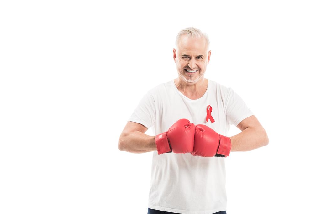 lachende volwassen man in het lege witte t-shirt met aids bewustzijn rood lint en bokshandschoenen geïsoleerd op wit, bestrijding van aids concept - Foto, afbeelding