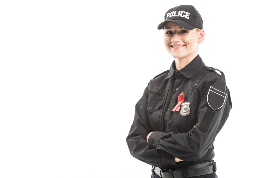 happy female police officer with aids awareness red ribbon looking at camera with crossed arms isolated on white - Photo, Image
