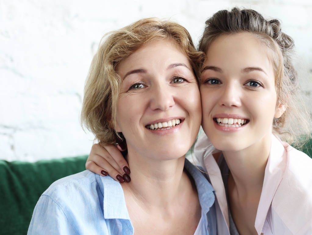 Beautiful senior mom and her adult daughter are hugging, looking at camera and smiling. - Photo, Image