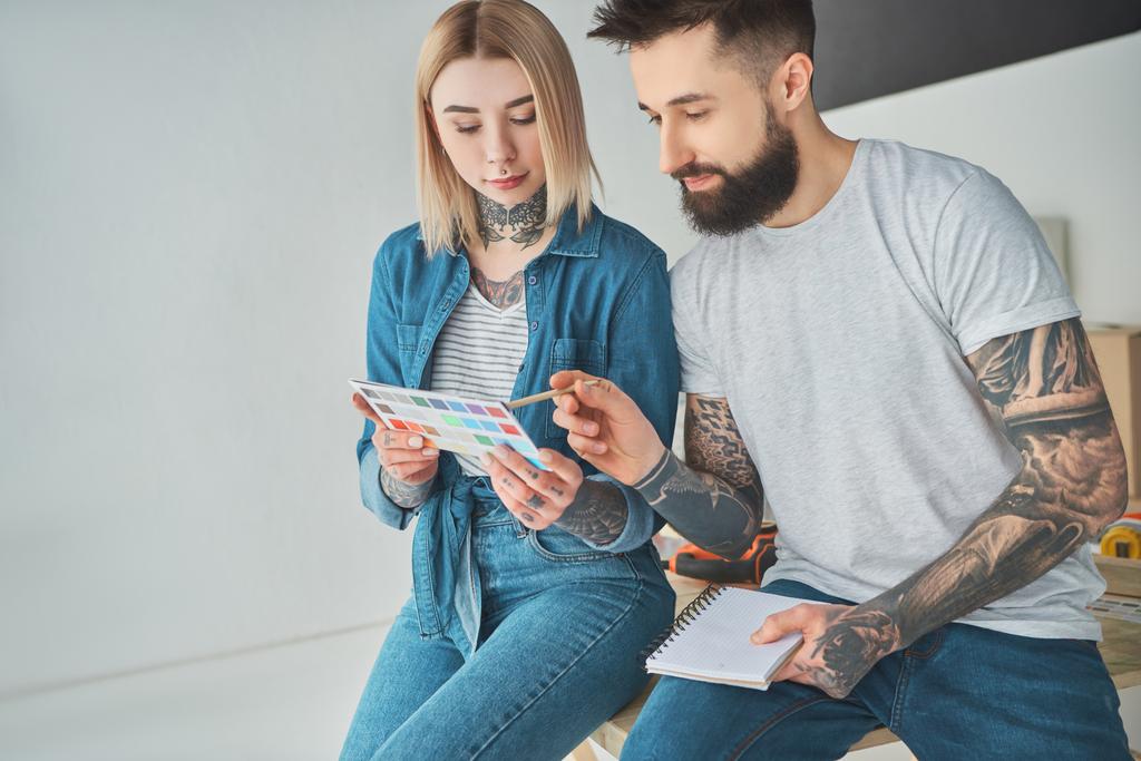 young tattooed couple holding palette of colors and choosing color for home improvement - Photo, Image