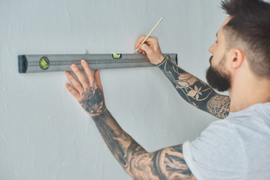 bijgesneden schot van jonge man houden niveau tool en markering muur met potlood tijdens reparaties - Foto, afbeelding