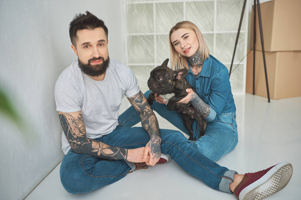 felice giovane coppia tatuata giocando con bulldog francese e sorridendo alla fotocamera nella nuova casa
 - Foto, immagini
