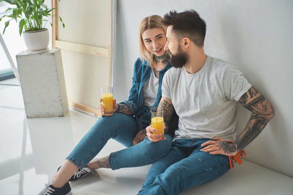 felice giovane coppia che tiene bicchieri di succo e seduto sul pavimento in una nuova casa
 - Foto, immagini